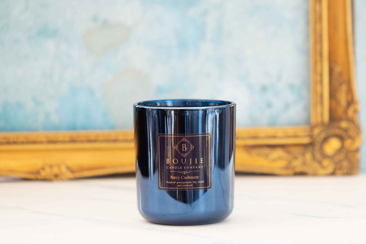 Boujie Navy Cashmere candle burning beside a gilt frame