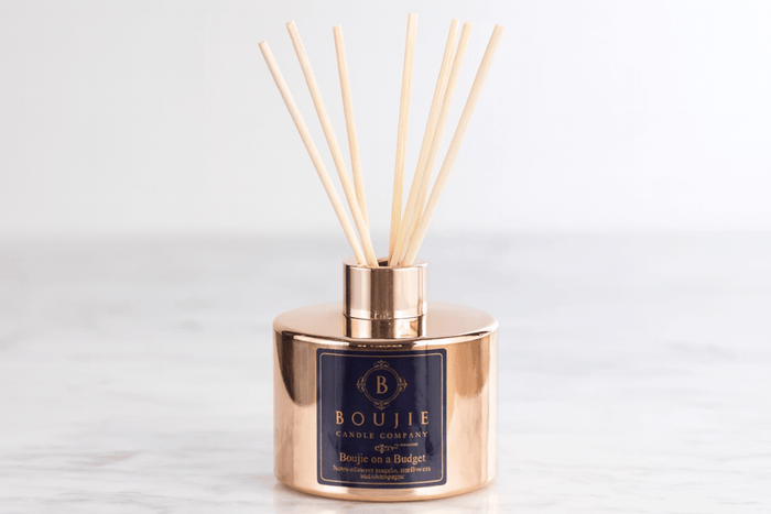 Boujie diffuser with rose gold cap and navy label on a light gray background