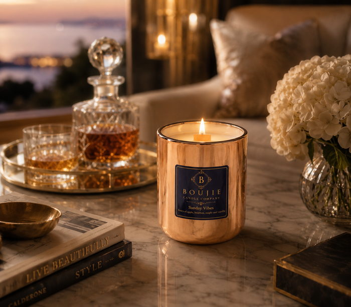 Boujie Sunday Vibes soy candle burning on a marble coffee table beside a bourbon decanter and white hydrangeas